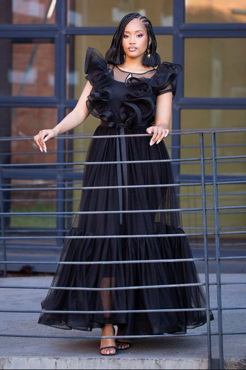Woman in a black ruffled dress standing in front of a metal fence.